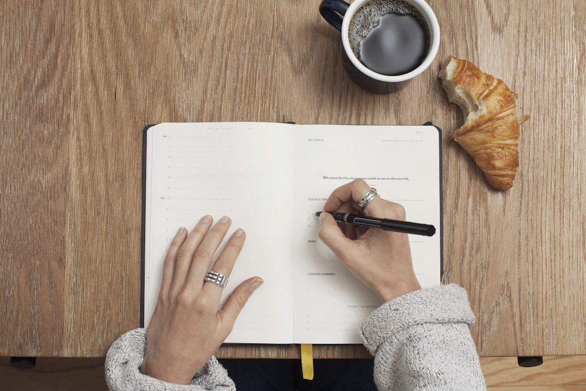 A person planning ideas in a notebook at a wooden table